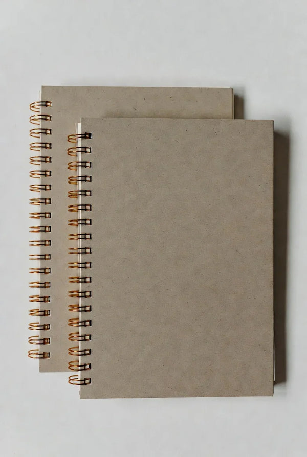 Two blank kraft paper spiral notebooks with copper wire binding on a white background