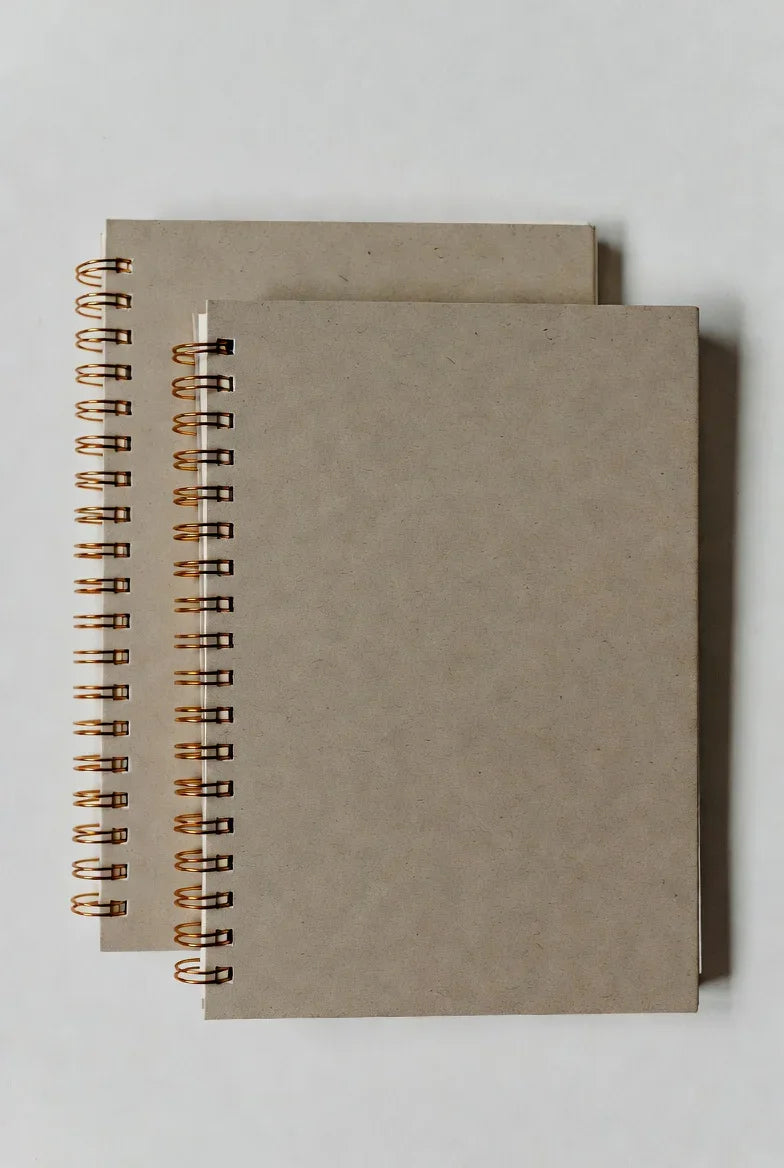 Two plain brown spiral notebooks with kraft covers on a white background