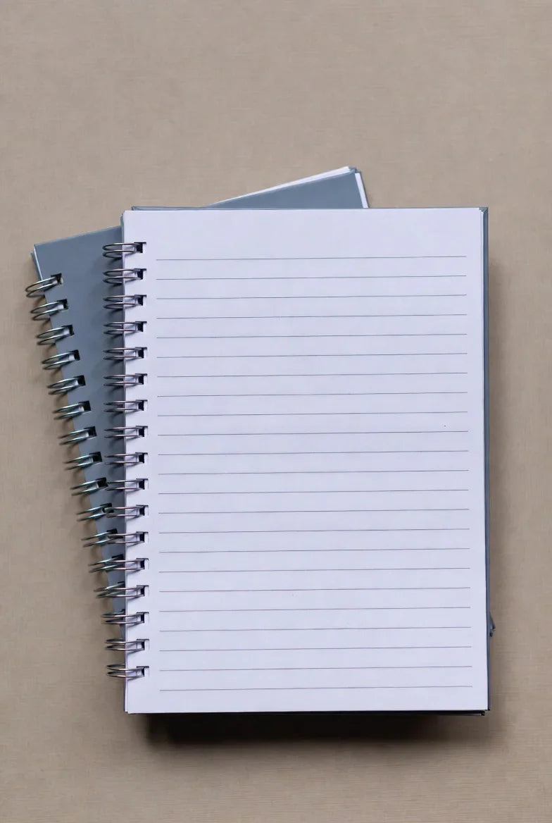 Two spiral bound notebooks with lined pages on a beige desk