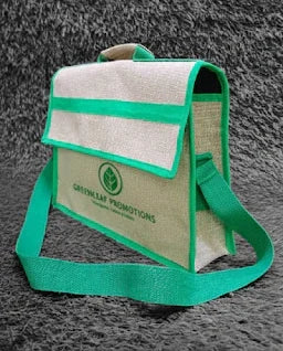 Eco-friendly jute sling bag with green trim and logo on gray textured background